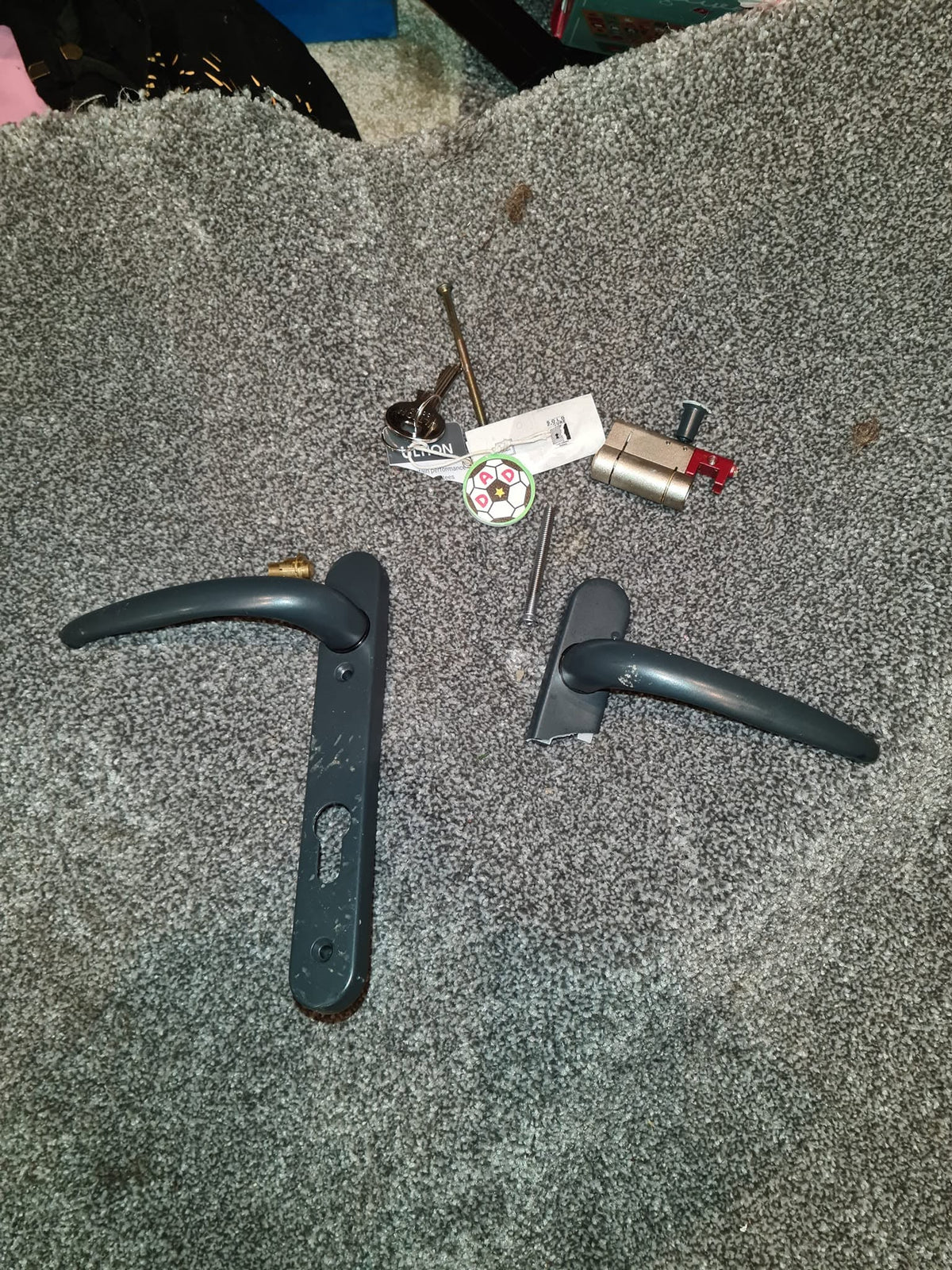 Damaged  door handle and cylinder parts laid on grey carpet after late night break-in 