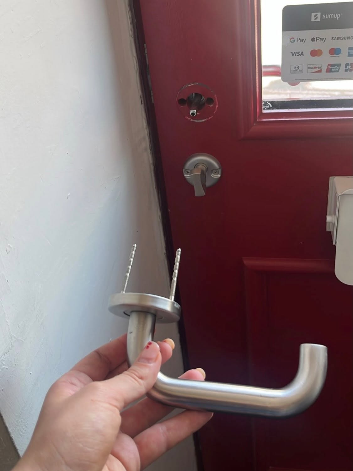 Broken chrome door handle being held up in front of red commercial door