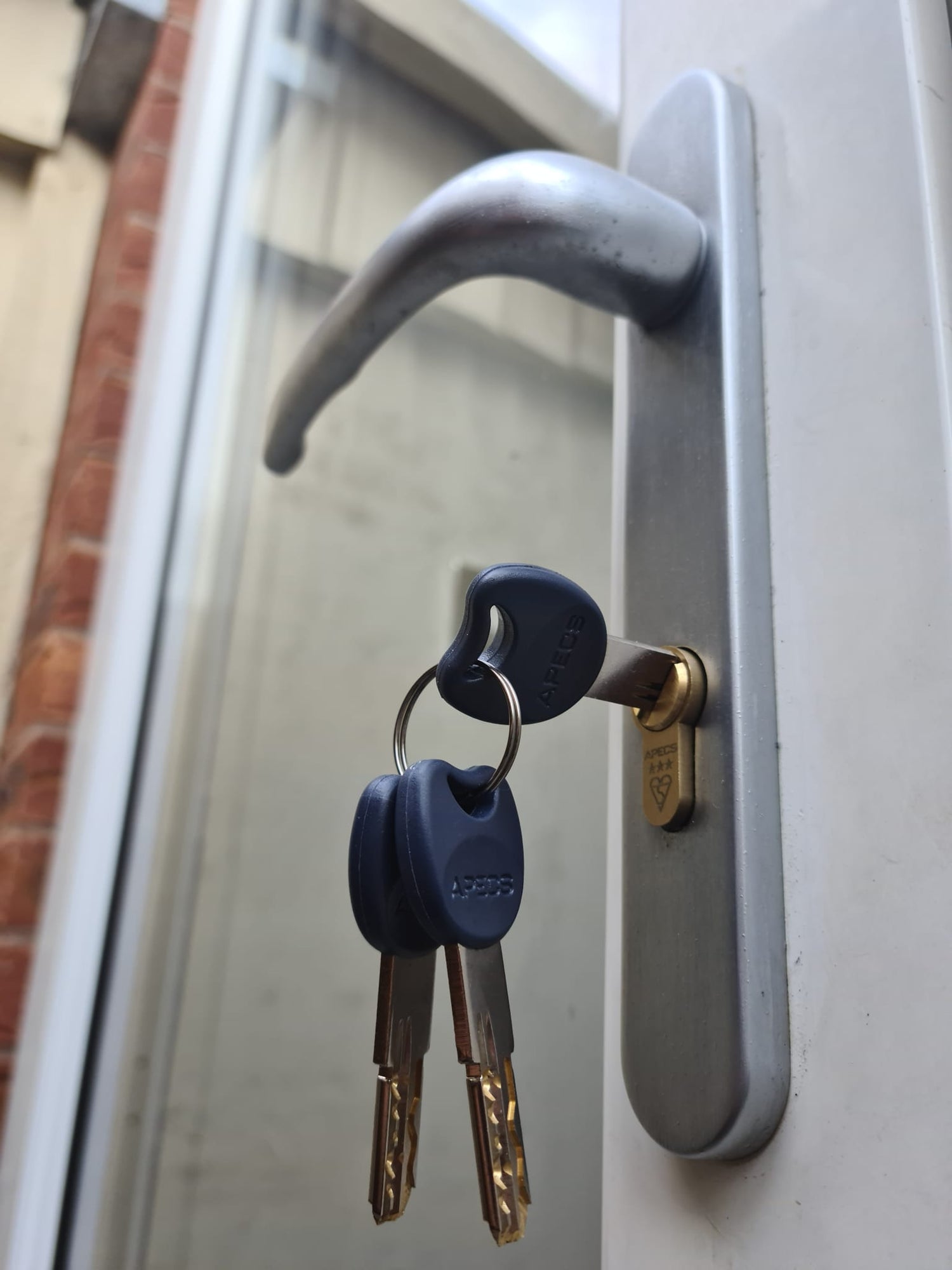High security replacement lock fitted to a silver door handle with one key in the lock and 2 keys on a keyring