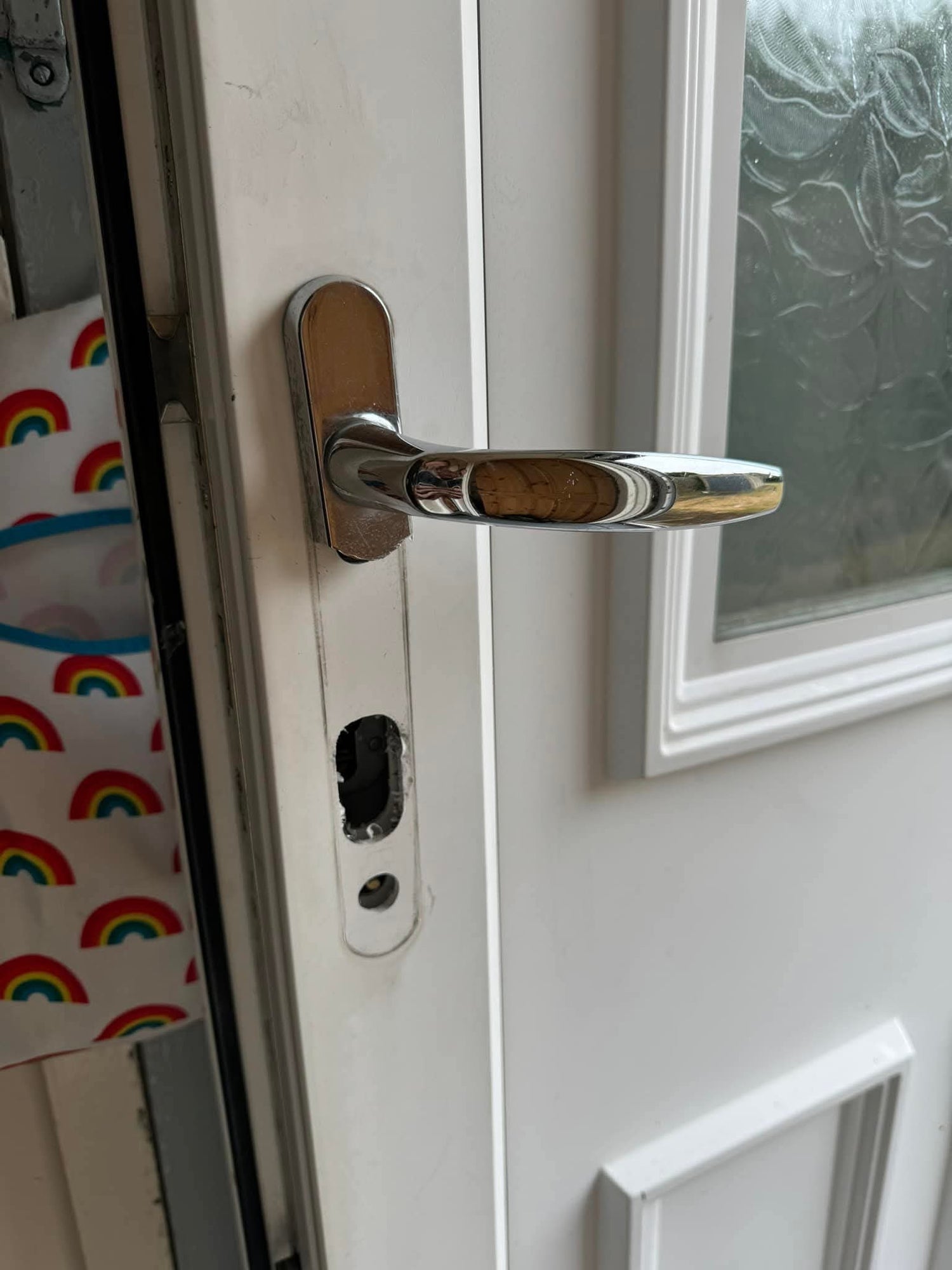 Close-up of a silver door handle after a lock snapping attack on a white door with a window.