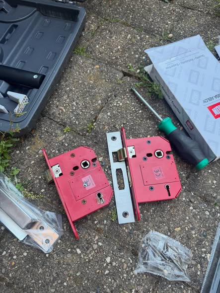 old and new red mortice locks laid on pavement with packaging and screwdriver 