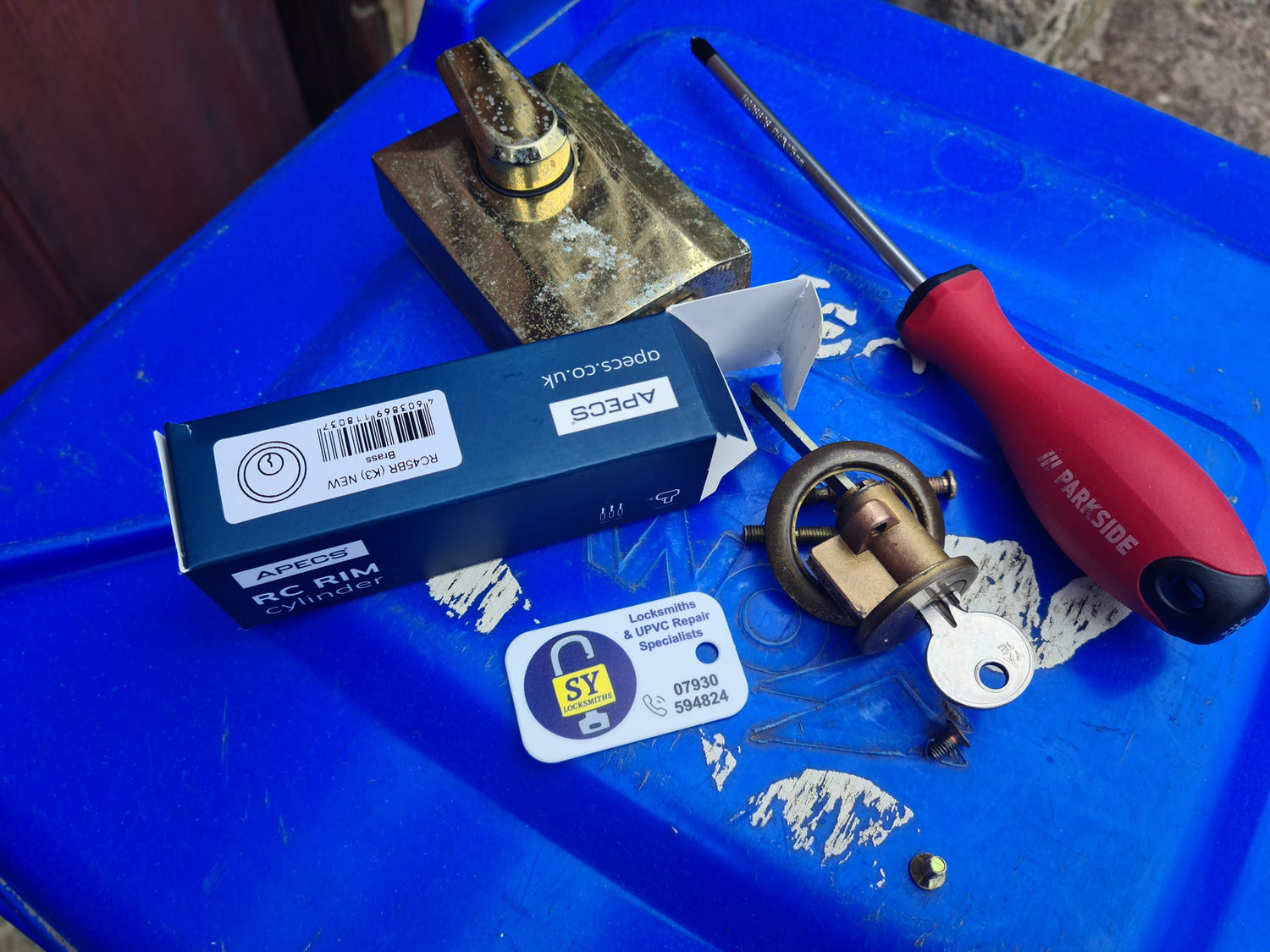 Mechanical night latch parts and tools on a blue surface during repair