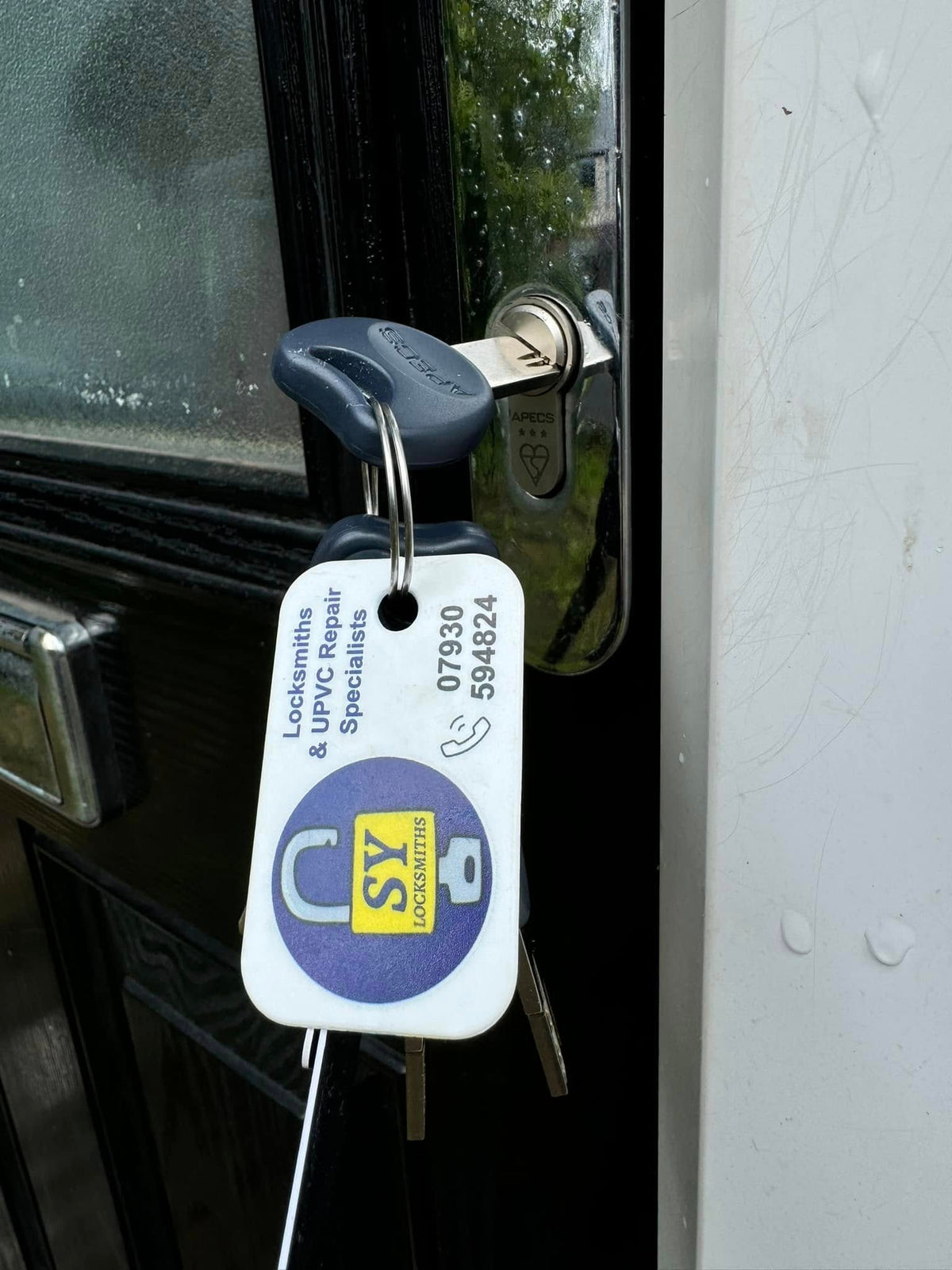 Replacement lock fitted to black composite door with key in the lock and SY Locksmiths key tag attached