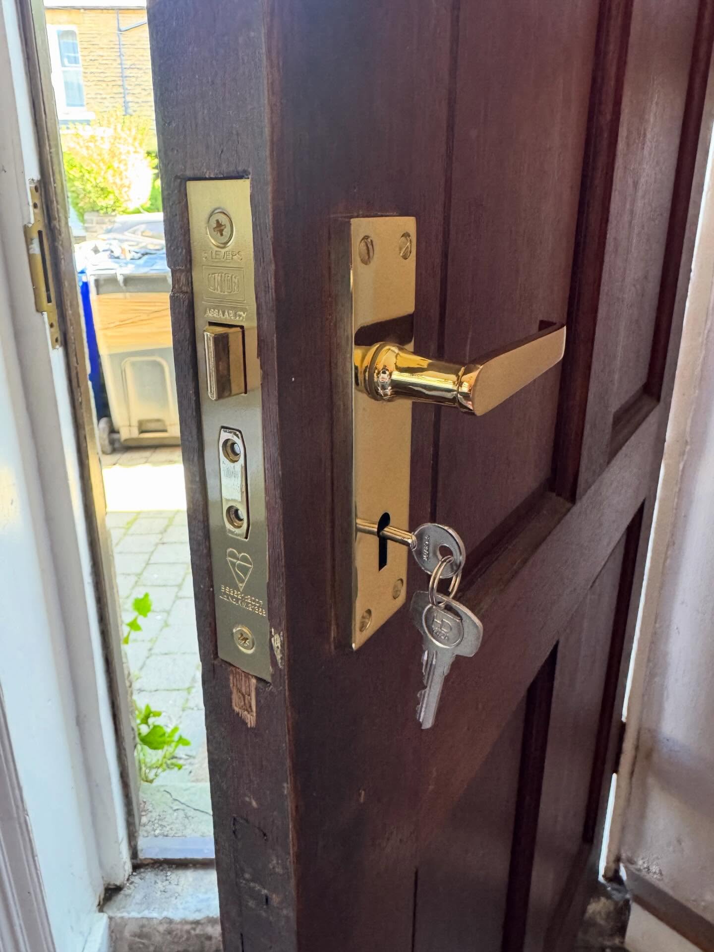 Brass coloured union sash lock fitted to brown wooden door with brass mortice lock handles and silver key 
