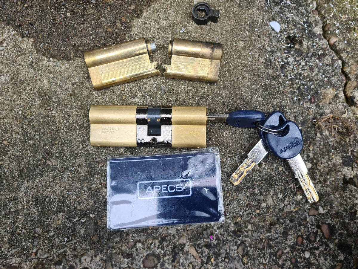 A basic brass euro lock snapped in half  laid on concreate next to a brass 3 star anti snap lock 