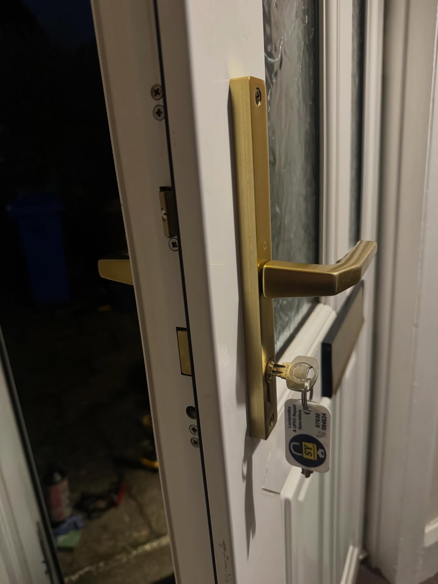 Close-up of a door handle with a key attached with SY Locksmiths branded key ring on a white upvc door.