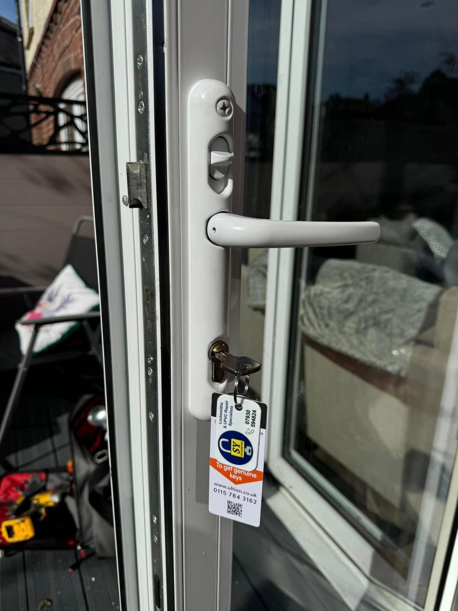 Close-up of a multi point lock on a white upvc with a white door handle with a key attached, set against a blurred outdoor background.