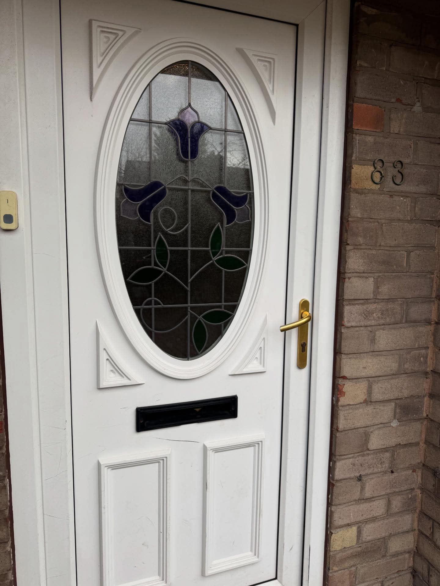 White door with decorative glass panel and gold handle on a brick wall.
