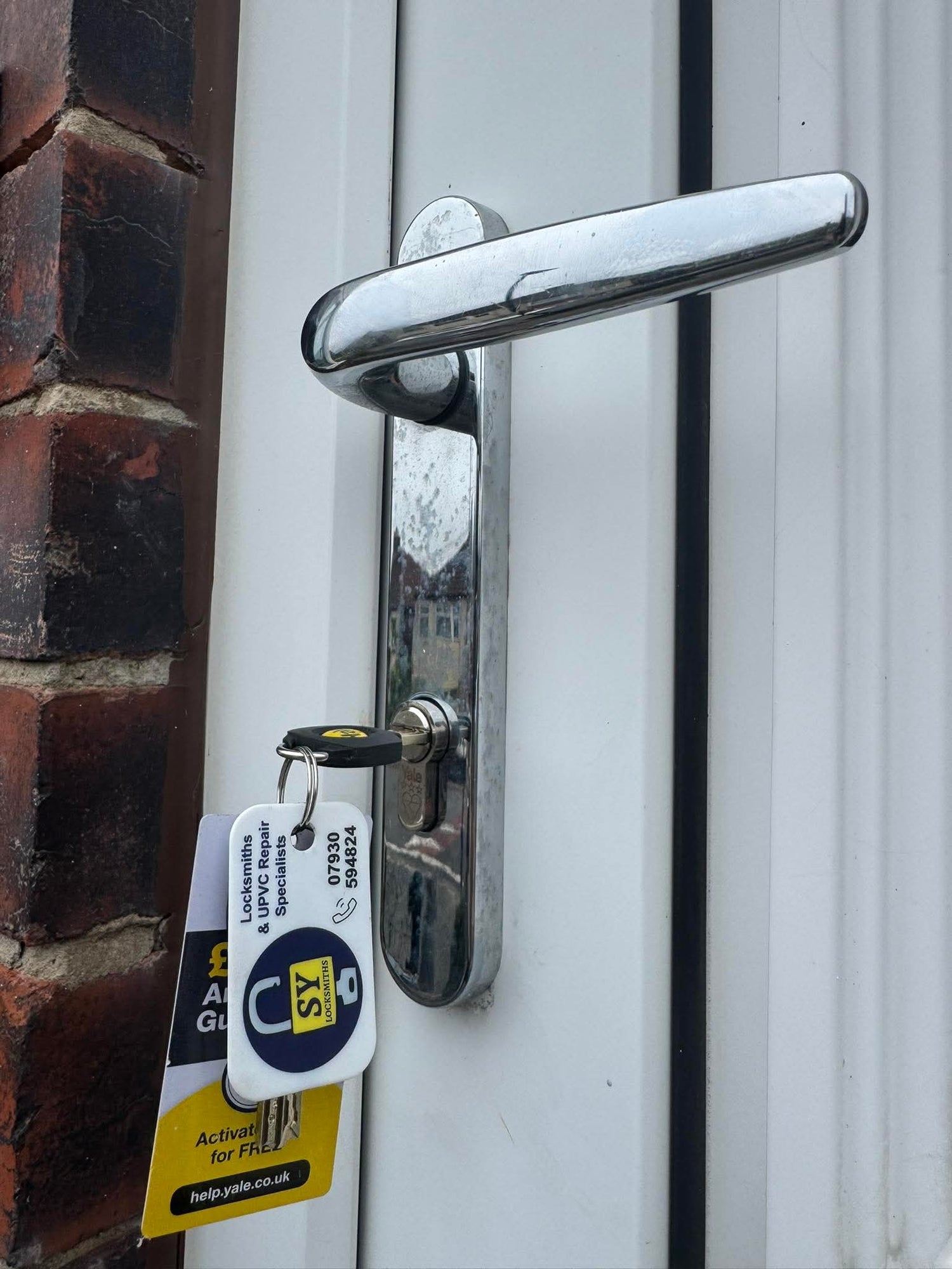 Metal door handle with a Yale 3 star anti snap lock a white door, next to a brick wall.