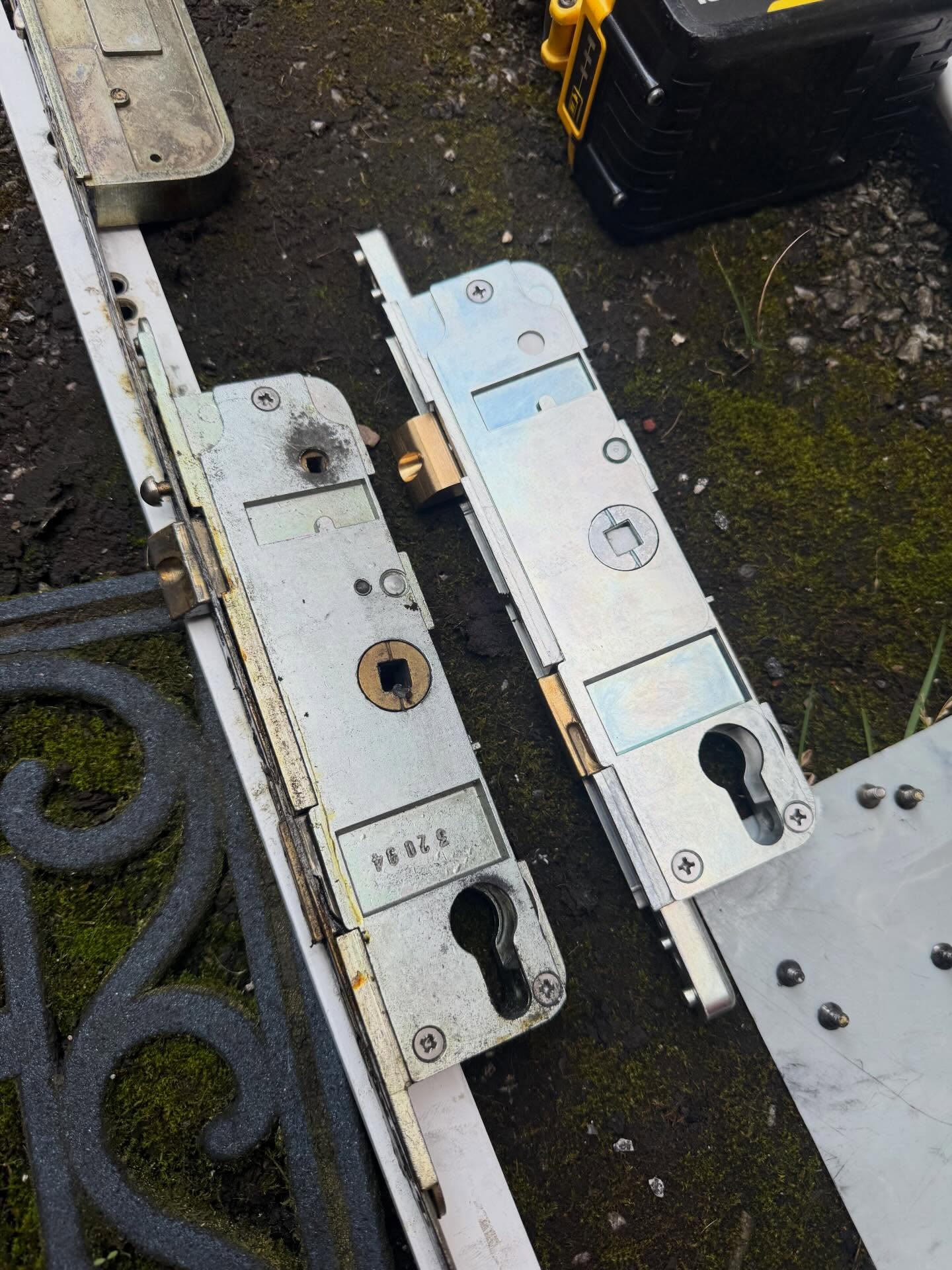 Metal multi point lock mechanism on a dark surface with tools in the background